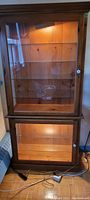 Full front view of the stained pine hutch showing upper and lower glass door compartments with lighting on inside.