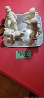 Four porcelain Snowbabies miniature figurines on a rectangular mirror base, showing their skating poses and textured suits.