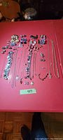 Full layout showing all 46 pieces spread on a red table including necklaces, bracelets, earrings, brooches, and pins.