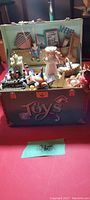 Front view of the open toy chest music box showing many miniature toys inside including a doll, spinning top, rocking horse, and circus-type backdrop