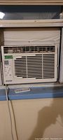 Window air conditioner installed in window with remote on window sill.