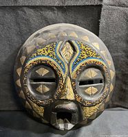 Front view showing complete circular wooden mask with beaded eye rims and brass accents.