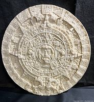 Full front view of the off-white round ceramic plaque with detailed Aztec sun stone calendar relief.