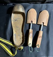 Brass left shoe showing worn surface and makeshift ankle tie next to pair of wooden shoe inserts.
