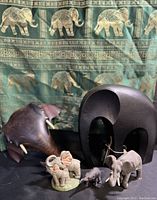 Photo showing various elephant figurines and sculptures in front of the green Thai silk elephant-patterned cloth.