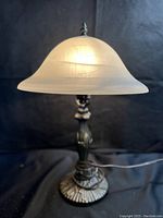 Table lamp lit to show glass shade and metal base with intricate details