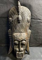 Front-side view showing the mask's facial features, geometric patterns, and raised dot detailing on dark wood.