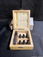 Open wooden box showing six hollow punch pieces and one handle inside foam cutouts.