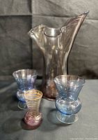 Collection of iridescent glassware including the two blue bulb glasses, the tall smoky iridescent vase and the small pink Bartlett Collins bud vase with gold stripes.