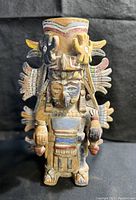 Front view of the Mayan South American urn sculpture, showing detailed face, headdress with wings, and painted clay design.