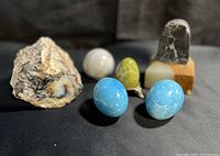 Overview of entire lot displaying petrified wood, blue eggs, green egg on stand, grey orb, and orb bookend on black fabric background with soft lighting.