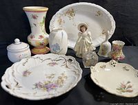 Full view of the porcelain and ceramic collectibles including vases, plates, figurine and lidded container.