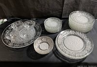 Full view of the entire 32-piece Princess House Fantasia pattern dishware collection arranged on a black surface. Includes plates, bowls, cups, and a large platter with clear and frosted leaf patterns.
