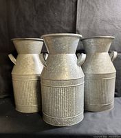 Three galvanized steel milk cans front view showing textured lower section, handles and flared tops.