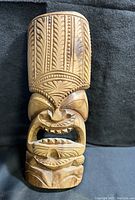 Front view of the wooden tiki statue showing full face and headdress details.