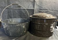 Photo showing two vintage graniteware pots side by side: blue speckled stock pot with wooden-handled wire bail and black speckled canning pot with lid.