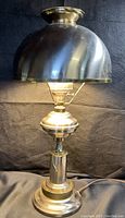 Full view of the vintage hurricane style lamp showing the lamp lit, with pewter shade and brass base, on a dark background.