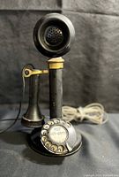 Front view of the vintage black candlestick rotary dial phone showing the rotary dial with phone number and separate handset.