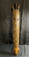 Front view of full length of wooden giraffe head mask showing carved spots and ears.
