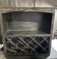 Front view of wooden wine rack showing open shelf on top and diagonal lattice to hold wine bottles below.