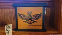 Photo of wooden box showing front panel with Haida indigenous bird design and signature.