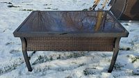 Full front view of La-Z-Boy outdoor coffee table on snow-covered grass showing wicker sides and glass top