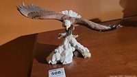 Porcelain eagle statue on base showing front and side views with wide wing span and details of feathers and base texture.