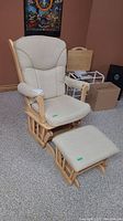 Frontal view of the wooden gliding rocker chair with removable beige cushion seated beside matching ottoman on carpeted floor.