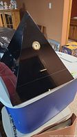 Full view of pyramid-shaped black ebony humidor with front-mounted hygrometer and visible small chip at the front bottom edge.