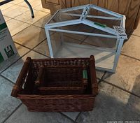 IKEA Socker greenhouse in white metal and glass with removable bottom tray and two wicker baskets with handles placed on tiled floor