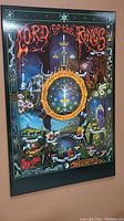 Framed Lord of the Rings illustrated poster board showing colorful fantasy scene with central ring symbol.