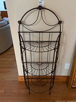 Front view of the three-tier metal plant shelf showing curved decorative top with chains and knots and three semi-circular wire shelves.