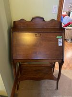 Front view of the solid wood secretary desk showing the curved top and closed pull-down panel with metal handle.