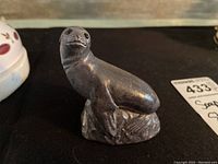 Front and side view of hand carved dark gray soap stone seal figurine on a black surface.