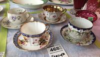 Four teacups with matching saucers arranged on table showing variety of floral and gold-trimmed designs