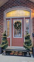 Full front shot of the front door decorated with two spiral artificial green Christmas trees in urn planters wrapped with gold mesh ribbon and a festive wreath on the door.