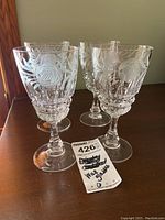 Four matching crystal wine glasses with etched patterns standing together on a wooden surface, showing overall lot.