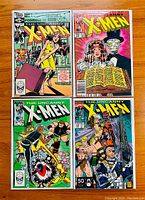 Four front covers of The Uncanny X-Men comic books on wooden surface showing vibrant Marvel comic art and characters such as Kitty Pryde and Sentinels.
