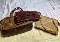 Three leather bags including two purses and one large bag, shown lying on white fabric background