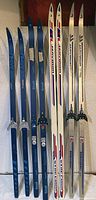 Photo showing six fiberglass Finnish cross country skis: three blue Karhu skis, three white Jrvinen skis with red and blue accents, all equipped with bindings and varying lengths.