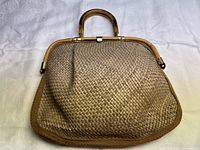 Front view of beige woven leather handbag with wooden handles laid flat on white background