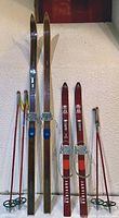 Photo showing two pairs of vintage wooden cross country skis in different sizes and colors along with four matching ski poles with round baskets and colored grips.