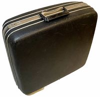 Front angled view of the vintage Samsonite black hard case suitcase showing black textured exterior, silver trim around edges, top handle, and worn condition.