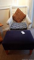 View of painted white wicker chair with brown pillow and black and white patterned cushion with navy blue upholstered ottoman in front