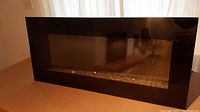 Front view of electric fireplace heater showing large black glass front with reflective surface and crystal-like decorative strip at the bottom inside edge.