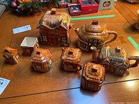 Overview of all pottery items displayed on wooden table showing multiple house-shaped containers and teapots.