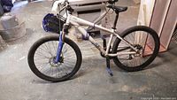 Side view of white and blue men's mountain bike with knobby tires, disc brakes, and front suspension fork.