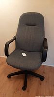 Front view of gray upholstered swivel office chair with armrests and caster wheels.