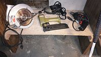 Full view of the four tools on a wooden shelf: Skilsaw circular saw, air-powered stapler, electric drill, and propane heater.