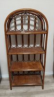 Front view of the wicker and rattan shelving unit showing four shelves and arched top.